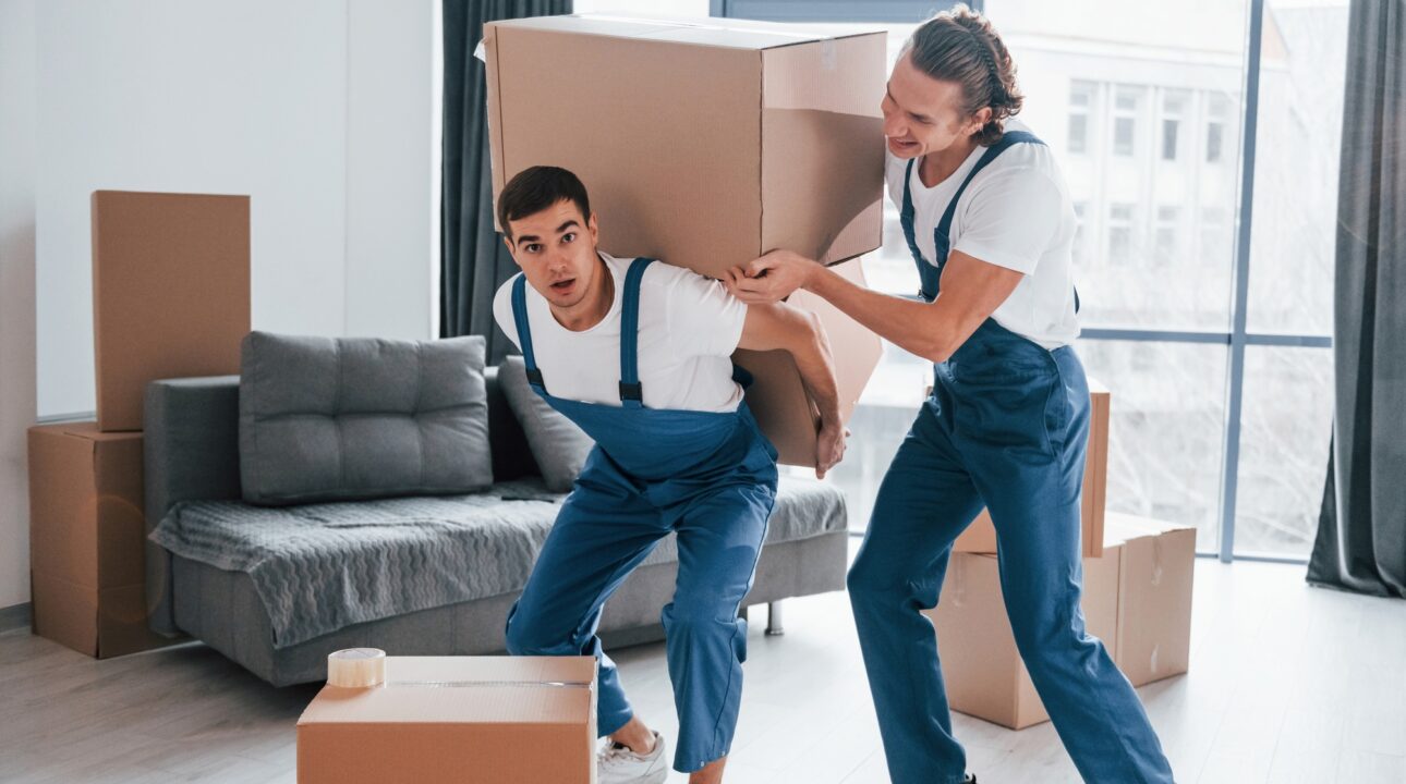 Home Services In Dubai 36 Heavy boxes. Two young movers in blue uniform working indoors in the room